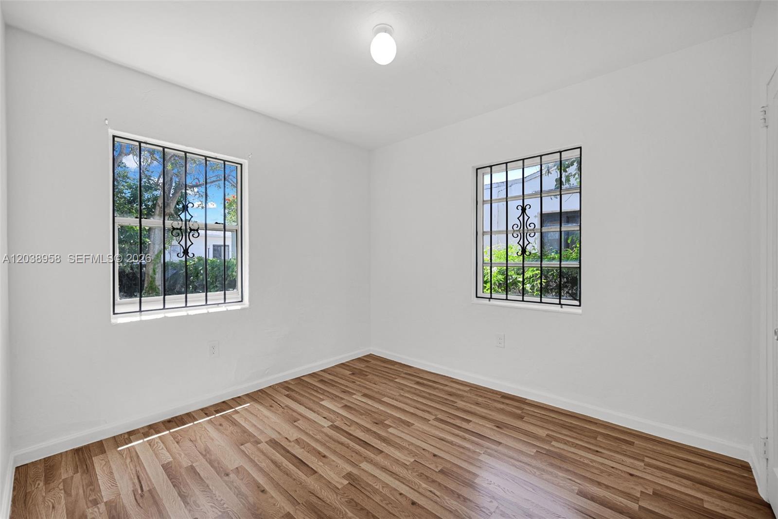 An empty bedroom features white walls, wood-look flooring, and windows with black security bars — 5511 NW 12th Ave, Miami FL 33127, MIAMI, FL