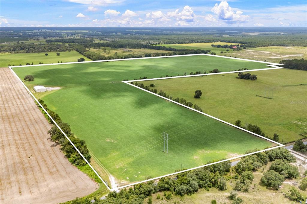 An aerial view shows a large, fenced-in green pasture with a small building and power lines — 7213 SW 298TH STREET, NEWBERRY, FL