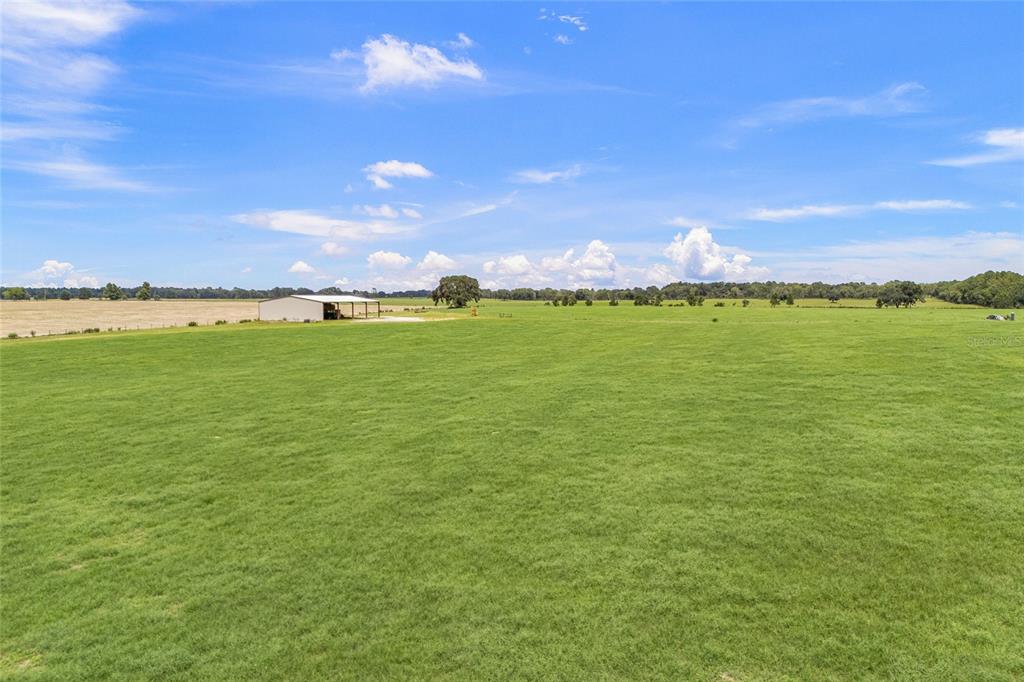 A large, flat green pasture features a metal barn under a bright blue sky — 7213 SW 298TH STREET, NEWBERRY, FL