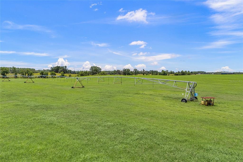 An agricultural center-pivot irrigation system stands in a large, open green pasture under a blue sky — 7213 SW 298TH STREET, NEWBERRY, FL