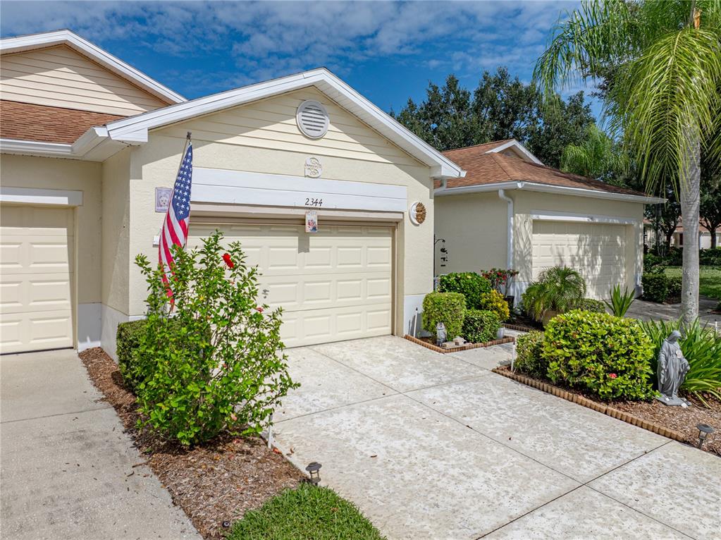 The exterior of a light yellow suburban home features a garage, driveway, and landscaping — 2344 NANTUCKET DRIVE UNIT 59, SUN CITY CENTER, FL