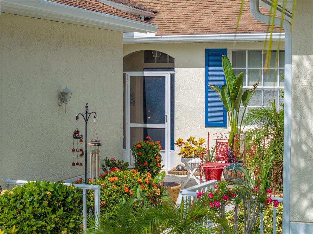 A front entryway features a screened door, a red metal chair, and potted plants — 2344 NANTUCKET DRIVE UNIT 59, SUN CITY CENTER, FL