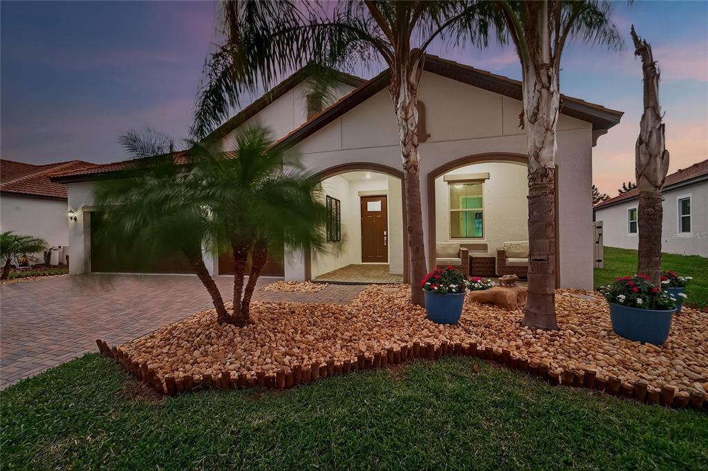 A single-story house exterior features a paved driveway, palm trees, and a covered front entryway — 16805 BANNER SHELL PLACE, WIMAUMA, FL