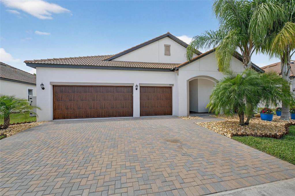 A single-story house with a paved driveway, two garage doors, and a palm tree — 16805 BANNER SHELL PLACE, WIMAUMA, FL