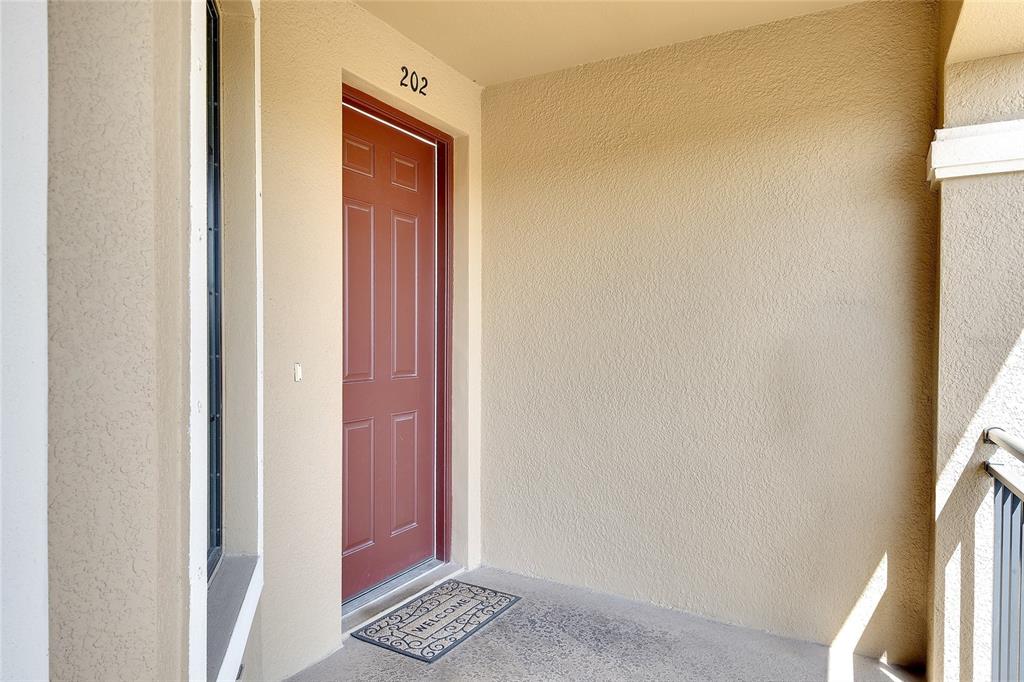 A red front door with the number 202 above it on a covered apartment balcony — 13608 MESSINA LOOP UNIT 202, BRADENTON, FL