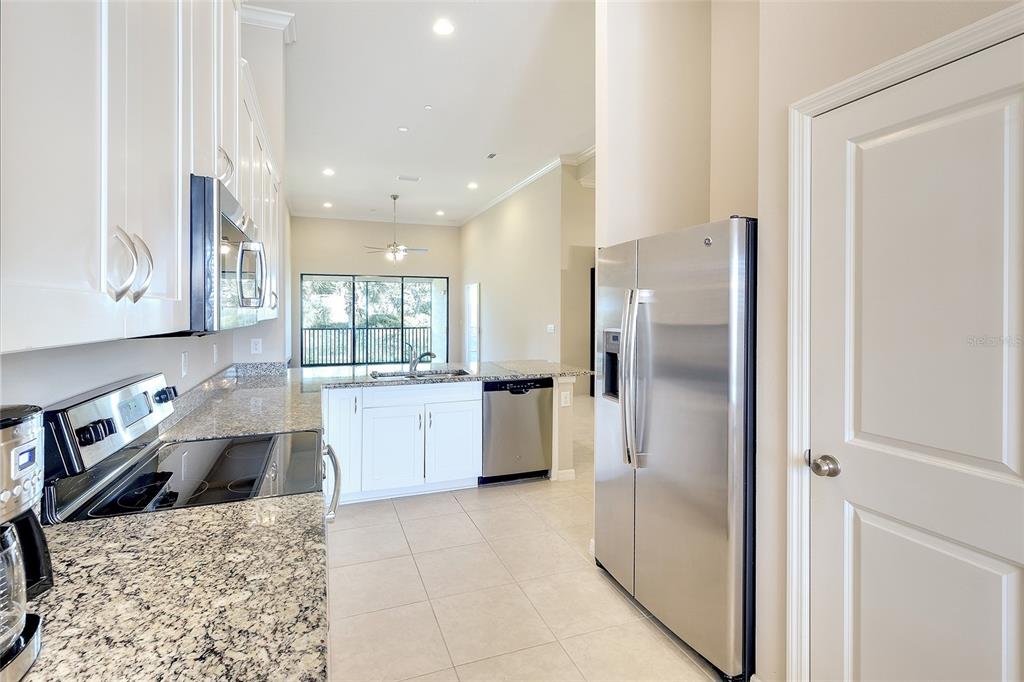 A kitchen with white cabinets, granite countertops, stainless steel appliances, and tile flooring — 13608 MESSINA LOOP UNIT 202, BRADENTON, FL