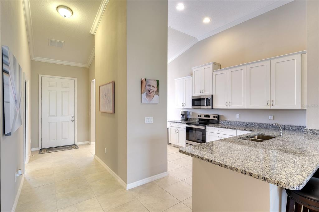 A view of a kitchen with granite countertops and white cabinets next to an entryway — 13608 MESSINA LOOP UNIT 202, BRADENTON, FL