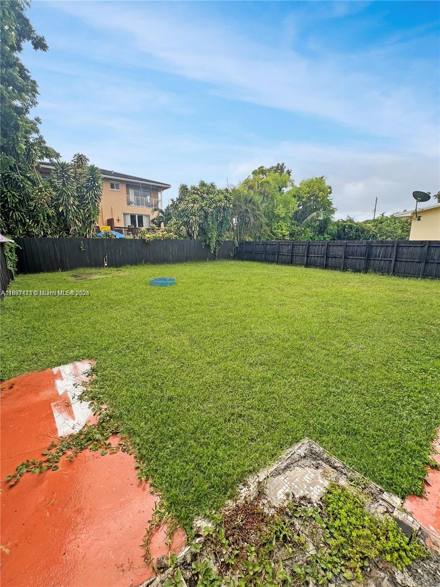 A large, grassy backyard is enclosed by a dark wooden fence under a blue sky — 2783 - 2785 SW 33rd Ct, Miami FL 33133, MIAMI, FL