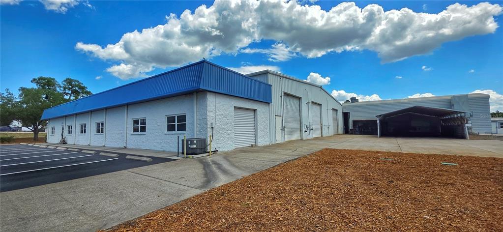 A white industrial building with a blue roof, roll-up doors, and an adjacent parking lot — 9324 EDEN AVENUE, HUDSON, FL