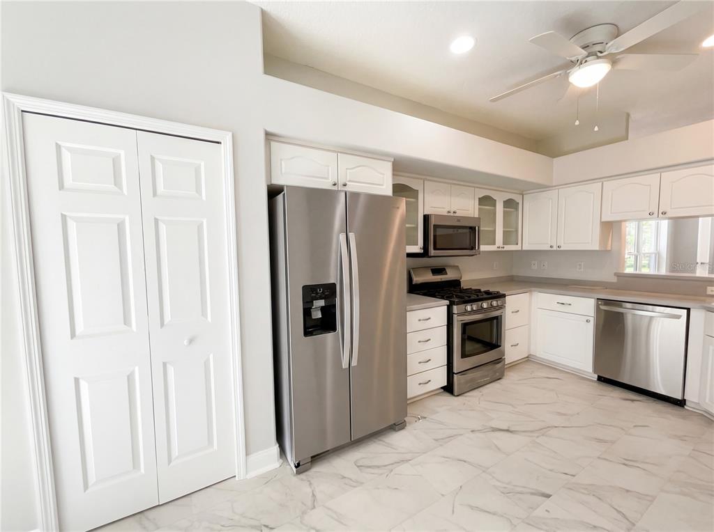 A kitchen features white cabinets, stainless steel appliances, and light-colored marble-patterned tile flooring — 5928 BRITTANIA BOULEVARD, TAVARES, FL