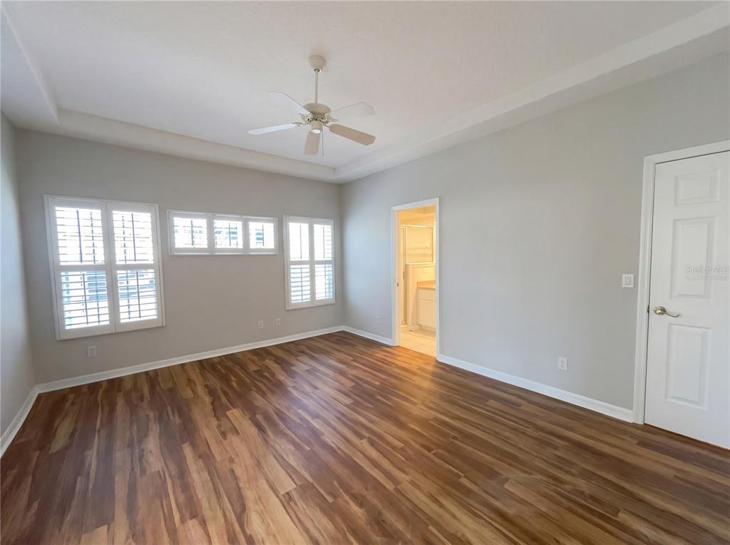 An empty bedroom features light gray walls, wood-look flooring, a ceiling fan, and white shutters — 5928 BRITTANIA BOULEVARD, TAVARES, FL