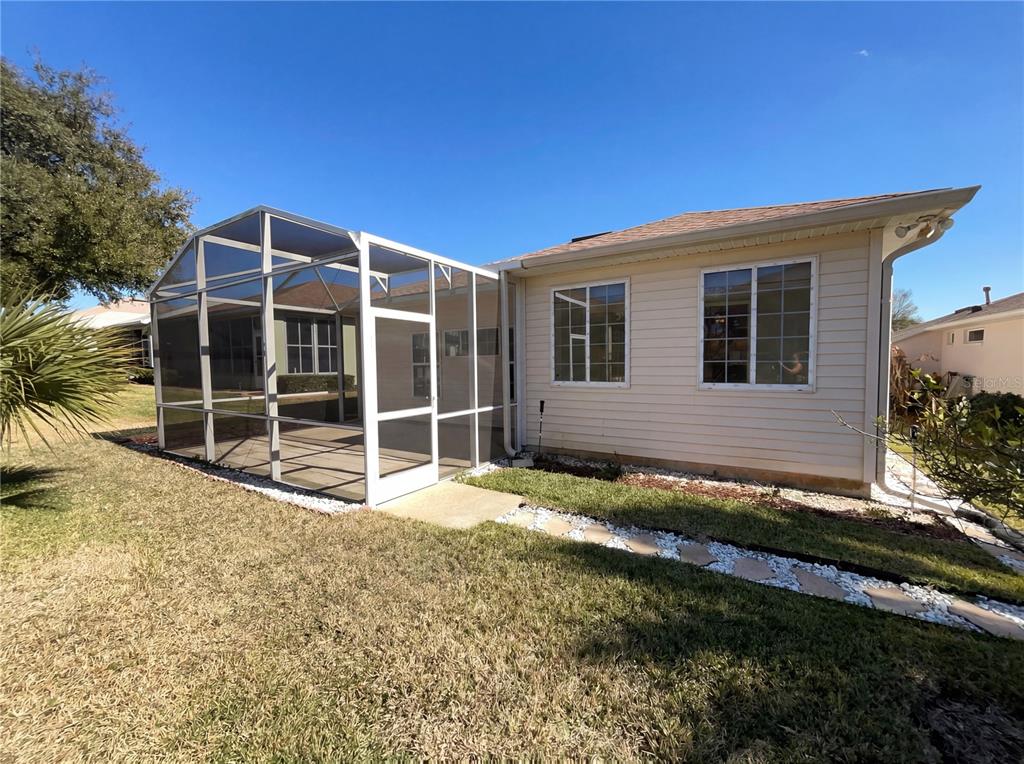 The exterior of a house features a screened-in patio, light siding, and a stone walkway — 5928 BRITTANIA BOULEVARD, TAVARES, FL