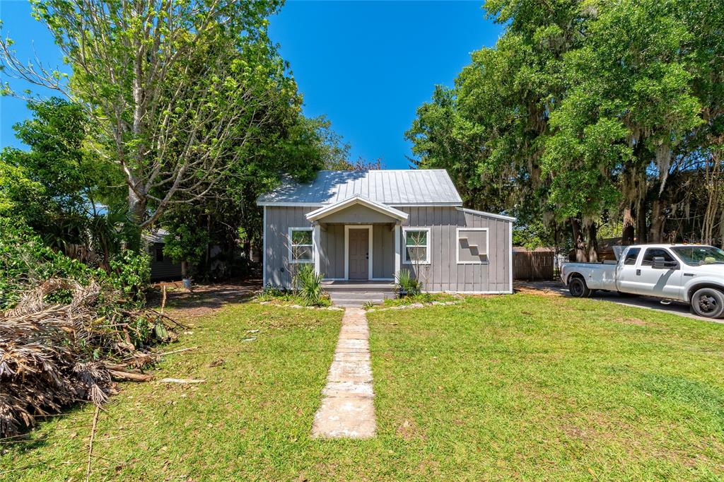 A single-story gray house with a metal roof sits behind a stone walkway and lawn — 714 WYOMING AVENUE, ST CLOUD, FL