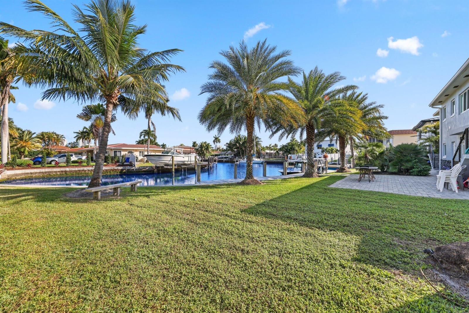 A grassy backyard features palm trees, a boat dock, and a paved patio by water — 830 SE 22nd Avenue, Pompano Beach FL 33062, POMPANO BEACH, FL