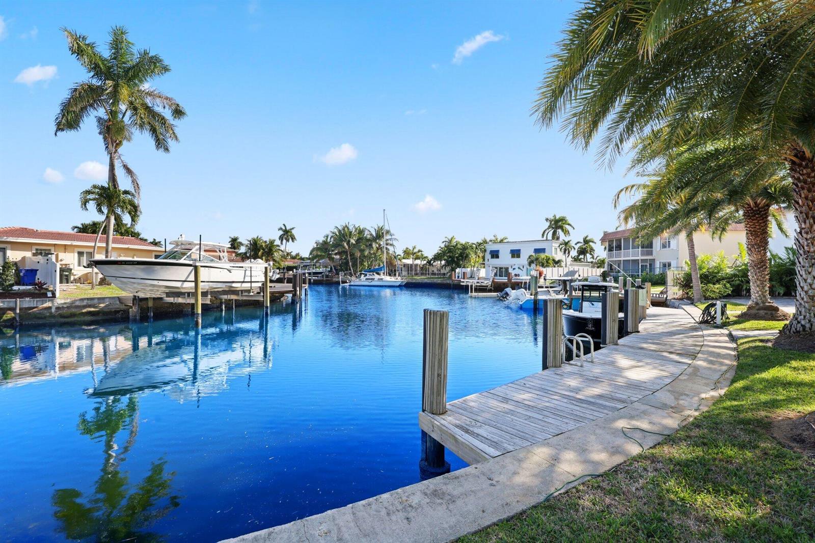 A canal view features a boat lift, a wooden dock, and palm trees under blue skies — 830 SE 22nd Avenue, Pompano Beach FL 33062, POMPANO BEACH, FL