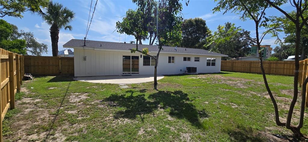 The backyard features a white house with a sliding glass door, patio, and wooden fencing — 965 VIGNOLES AVENUE NE UNIT 1, PALM BAY, FL