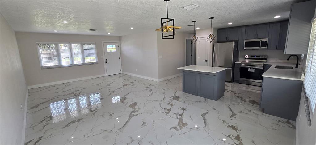An open-concept kitchen and living area features gray cabinets, stainless steel appliances, and marble-patterned tile — 965 VIGNOLES AVENUE NE UNIT 1, PALM BAY, FL