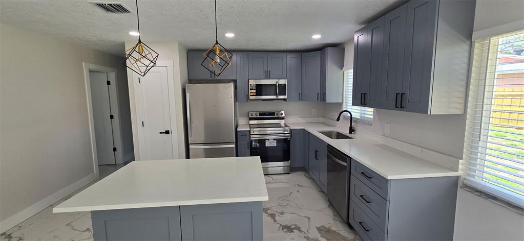 A kitchen features blue cabinets, white countertops, stainless steel appliances, and a central island — 965 VIGNOLES AVENUE NE UNIT 1, PALM BAY, FL