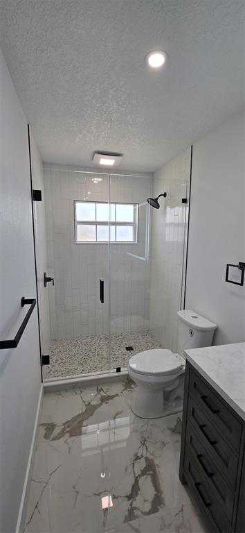 A modern bathroom features a glass-enclosed walk-in shower, a white toilet, and marble-patterned tile flooring — 965 VIGNOLES AVENUE NE UNIT 1, PALM BAY, FL