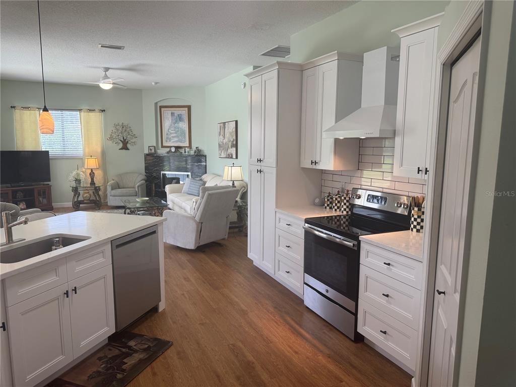A kitchen with white cabinets and stainless steel appliances opens into a living room area — 7102 42ND COURT E, SARASOTA, FL
