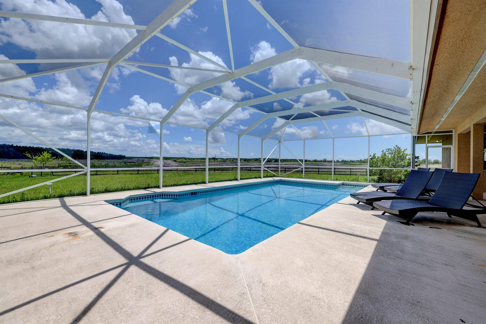 A swimming pool with a screened enclosure overlooks a grassy field under a blue sky — 2700 S Header Canal Road, Fort Pierce FL 34945, FORT PIERCE, FL