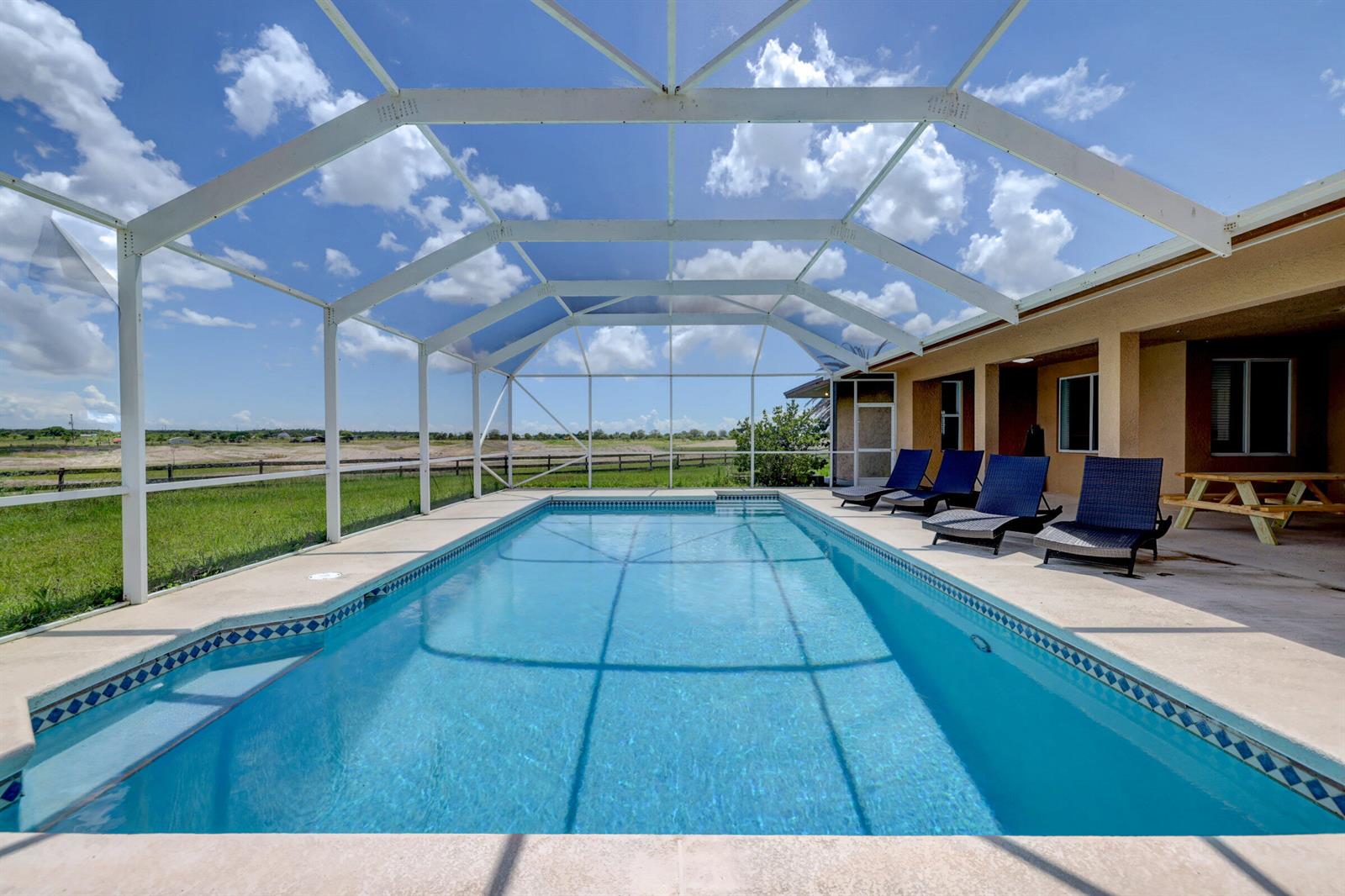 A rectangular swimming pool with a screened enclosure overlooks a grassy field — 2700 S Header Canal Road, Fort Pierce FL 34945, FORT PIERCE, FL
