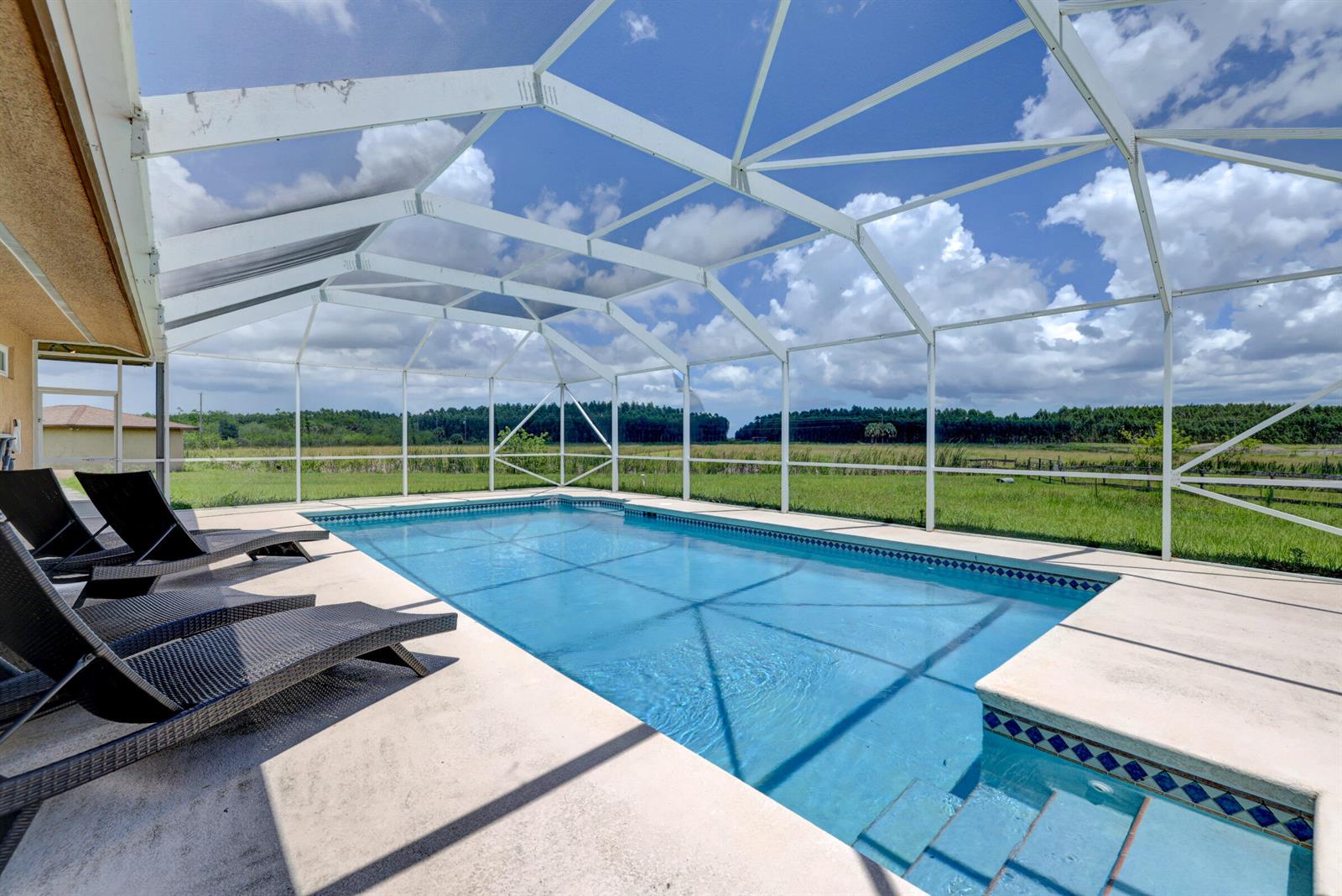 A screened-in swimming pool with lounge chairs sits on a patio overlooking a grassy field — 2700 S Header Canal Road, Fort Pierce FL 34945, FORT PIERCE, FL