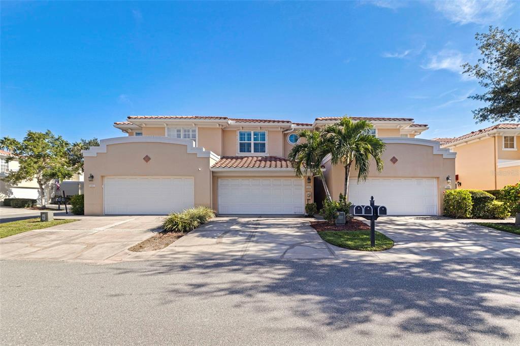 A two-story tan stucco townhouse with three white garage doors and a tile roof — 123 VALENCIA CIRCLE, ST PETERSBURG, FL