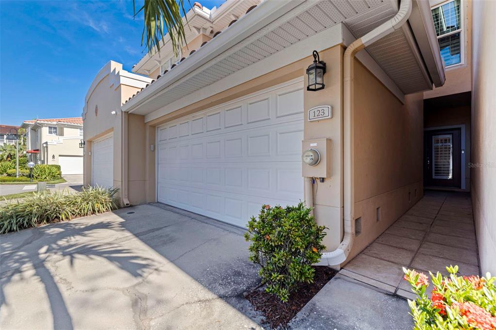 The exterior of a beige townhouse features a two-car garage, a side entrance, and landscaping — 123 VALENCIA CIRCLE, ST PETERSBURG, FL
