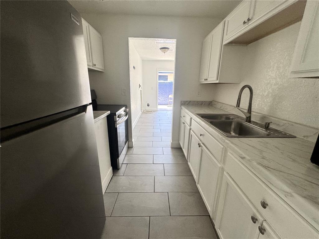 A galley kitchen features white cabinets, marble-look countertops, stainless steel appliances, and gray tile flooring — 6619 S WEST SHORE BOULEVARD UNIT A, TAMPA, FL