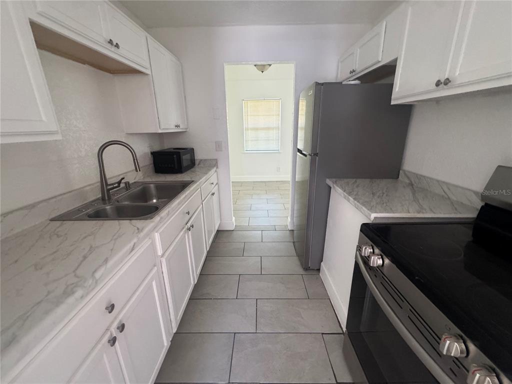 A galley kitchen features white cabinets, marble-look countertops, stainless steel appliances, and gray tile flooring — 6619 S WEST SHORE BOULEVARD UNIT A, TAMPA, FL