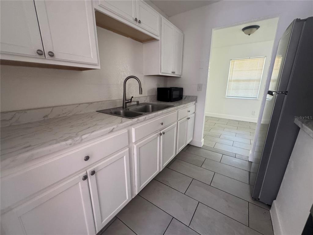 A kitchen features white cabinets, marble-look countertops, a stainless steel sink, and gray tile flooring — 6619 S WEST SHORE BOULEVARD UNIT A, TAMPA, FL
