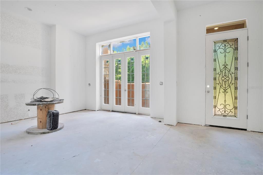 An unfinished room features white walls, concrete flooring, a glass-paned door, and French doors — 818 LAKE AGNES DRIVE, POLK CITY, FL