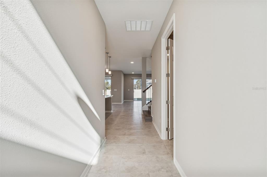 A tiled hallway leads toward an open kitchen and a staircase in a modern home — 5808 FREESIA DRIVE, LAKELAND, FL