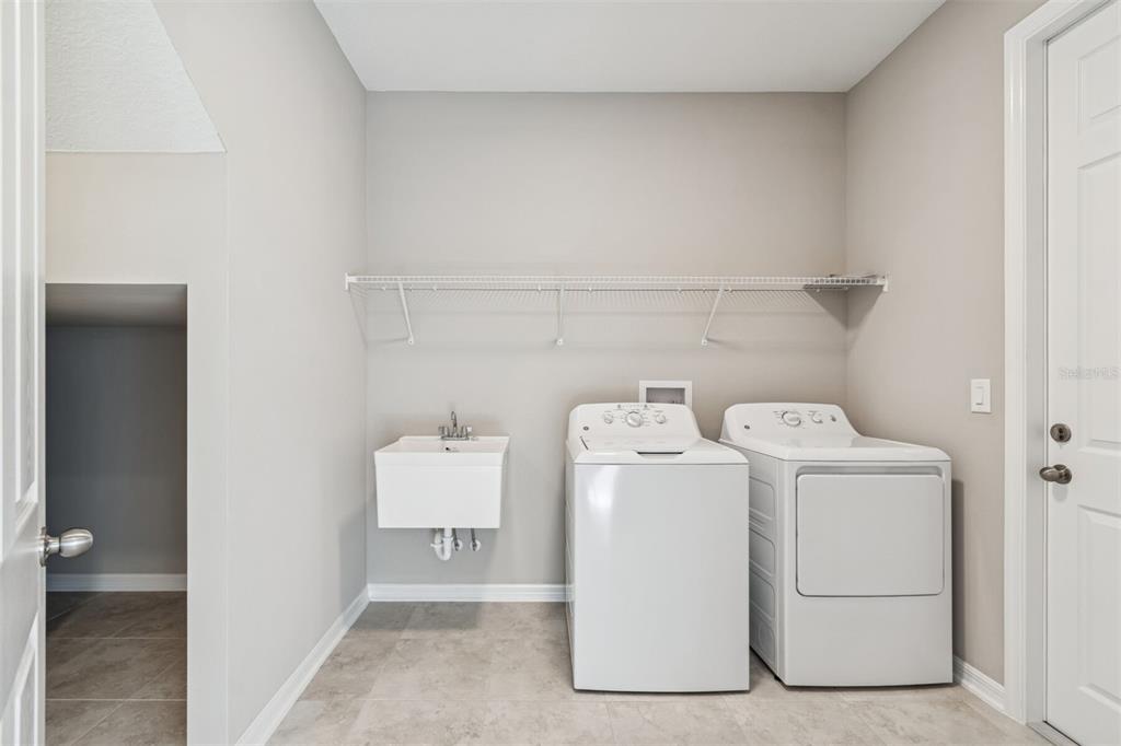 A laundry room featuring a utility sink, washer, dryer, wire shelving, and light gray walls — 5808 FREESIA DRIVE, LAKELAND, FL