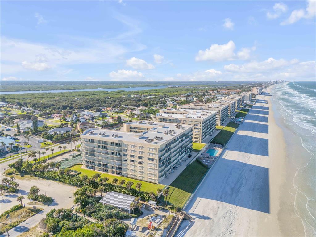 An aerial view shows beachfront condominium buildings with a pool and adjacent coastal landscape — 4575 S ATLANTIC AVENUE UNIT 6402, PONCE INLET, FL