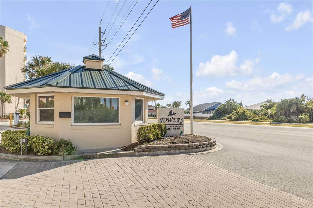 A guard shack with a metal roof stands next to a sign for Towers at Ponce Inlet — 4575 S ATLANTIC AVENUE UNIT 6402, PONCE INLET, FL