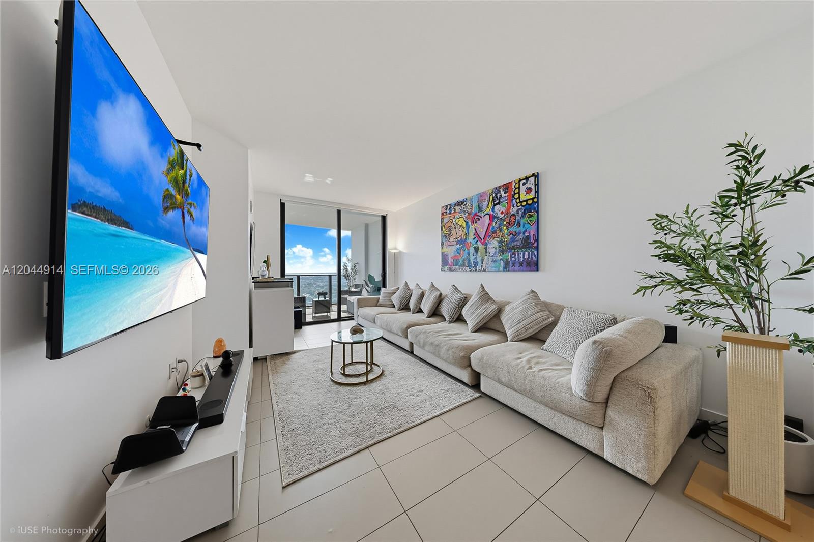 A living room features a large sectional sofa, a wall-mounted television, and a balcony view — 1600 NE 1st Ave # 2814, Miami FL 33132, MIAMI, FL