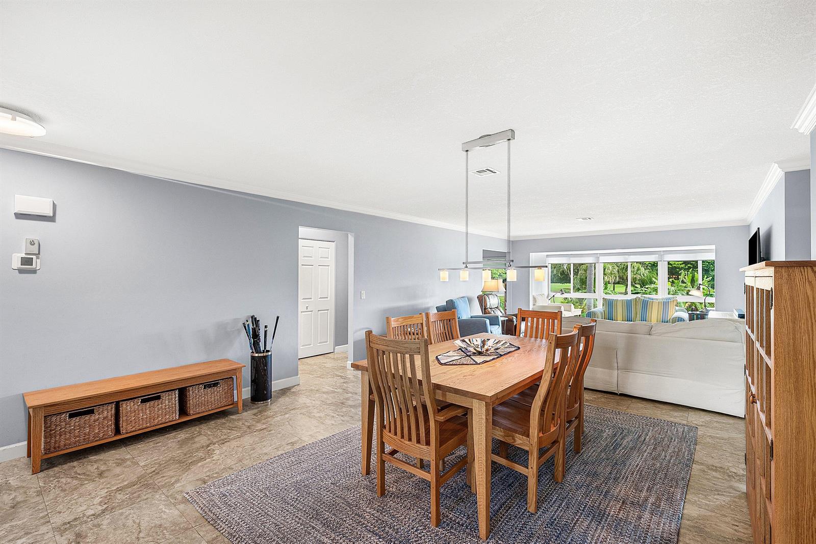 A dining area with a wooden table and chairs sits on a rug near a living room — 11212 Quail Covey Road, Boynton Beach FL 33436, BOYNTON BEACH, FL