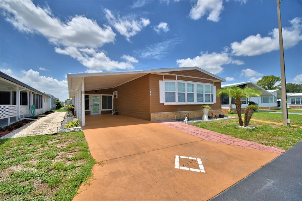A single-story manufactured home with a brown exterior, a carport, and a paved driveway — 4146 SPRUCEWOOD STREET, WINTER HAVEN, FL