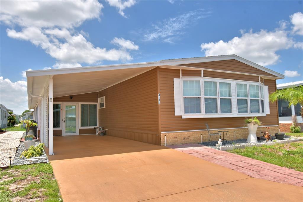 A tan mobile home features a large carport, a bay window, and a paved driveway — 4146 SPRUCEWOOD STREET, WINTER HAVEN, FL