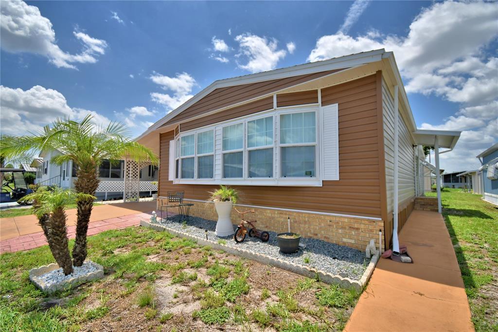 A tan-sided manufactured home features a bay window, brick skirting, and a paved walkway — 4146 SPRUCEWOOD STREET, WINTER HAVEN, FL