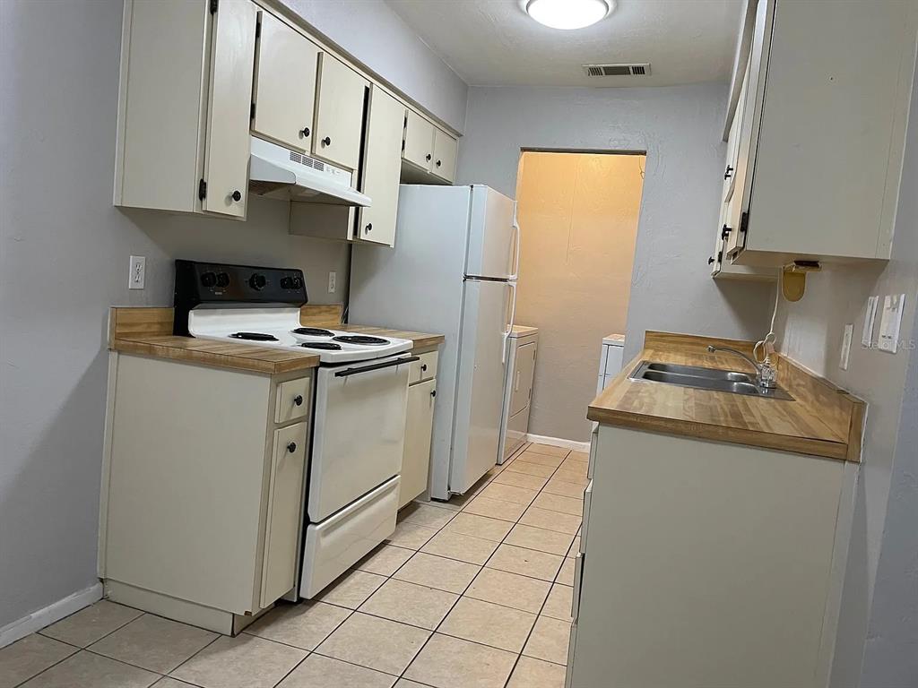 A galley-style kitchen features off-white cabinets, wood-look laminate countertops, and white appliances — 2210 SW 70TH TERRACE, GAINESVILLE, FL