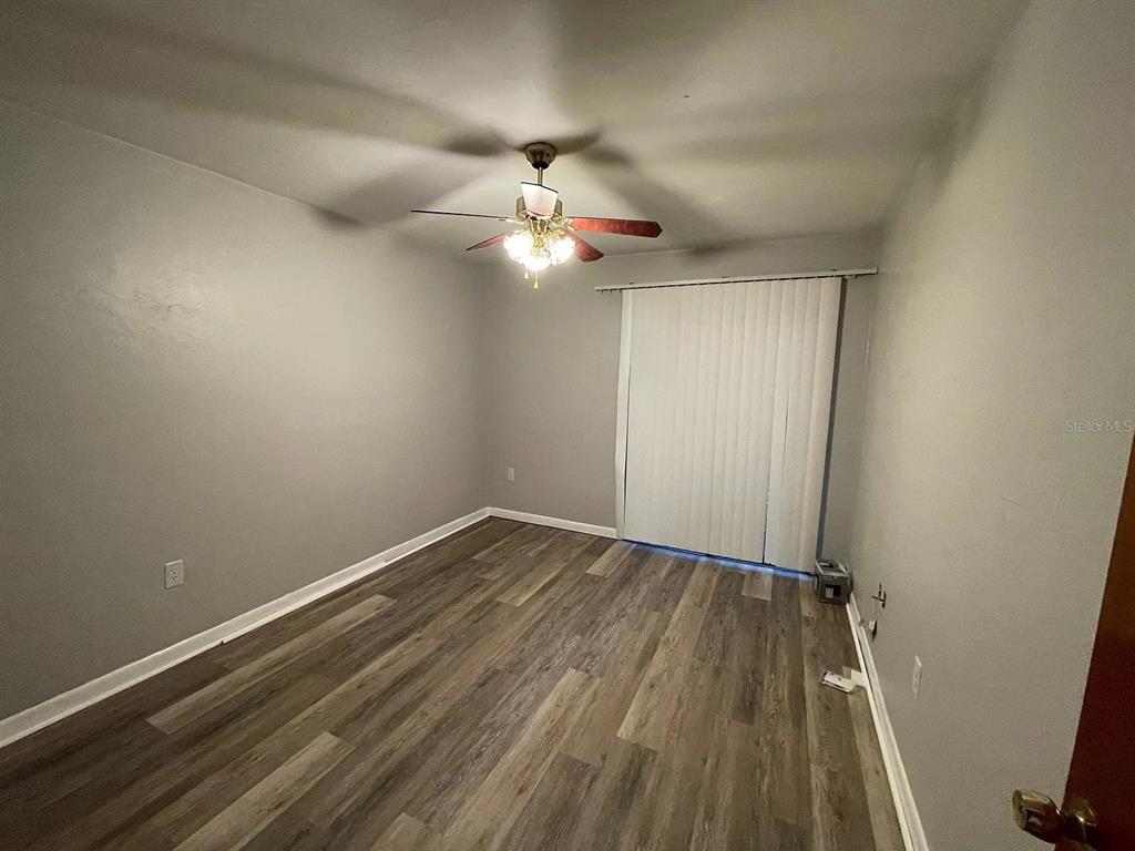 An empty room features gray walls, wood-look flooring, a ceiling fan, and vertical window blinds — 2210 SW 70TH TERRACE, GAINESVILLE, FL