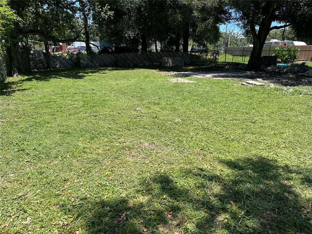A large, grassy backyard features a chain-link fence and mature trees under a sunny sky — 129 1ST STREET, WINTER HAVEN, FL