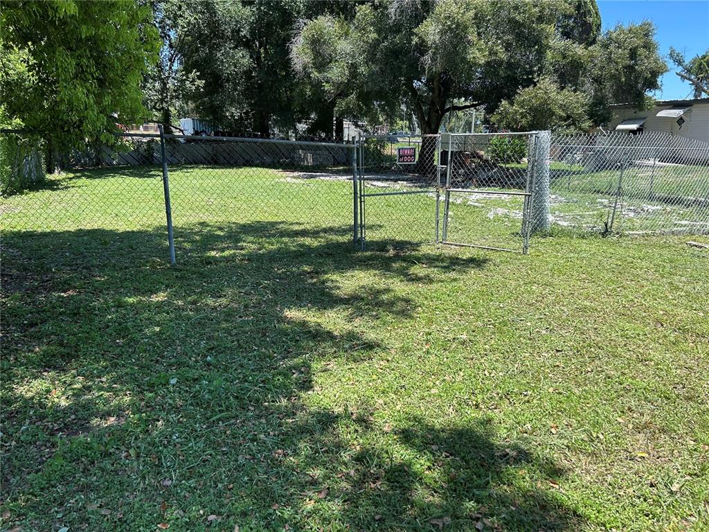 A chain-link fence encloses a grassy backyard with a gated entrance and mature trees — 129 1ST STREET, WINTER HAVEN, FL