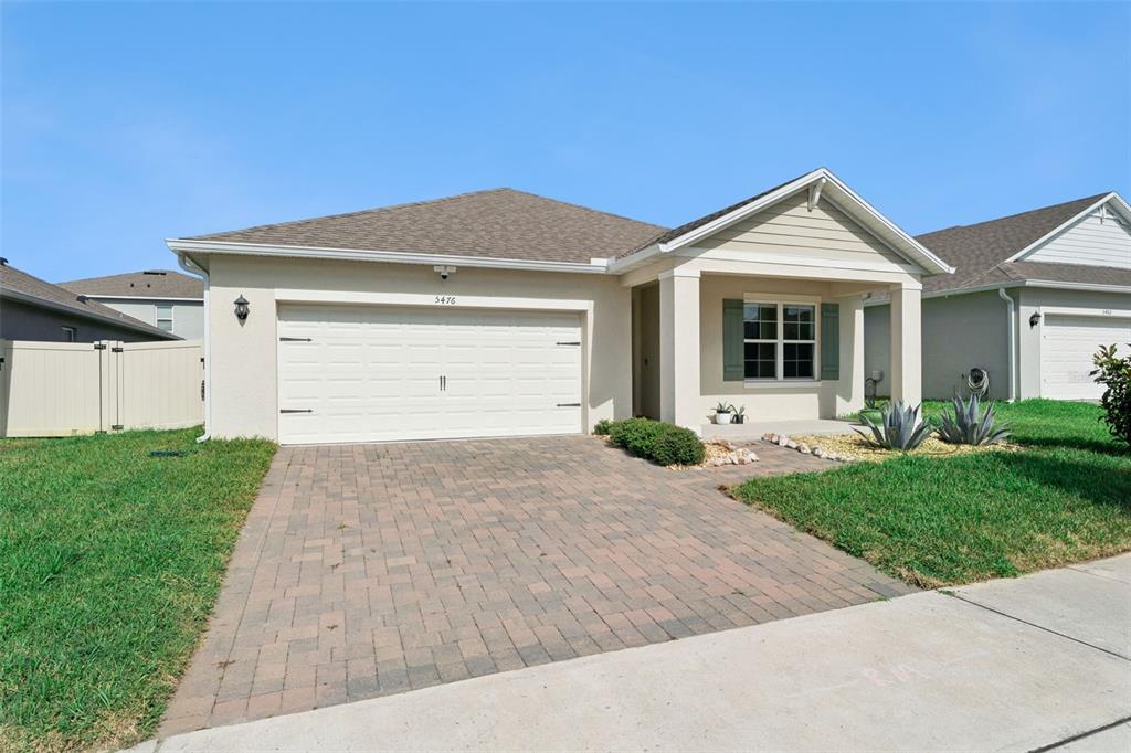 A single-story house features a tan stucco exterior, a paved driveway, and a covered entryway — 5476 HUNTER JUMPER LANE, APOPKA, FL
