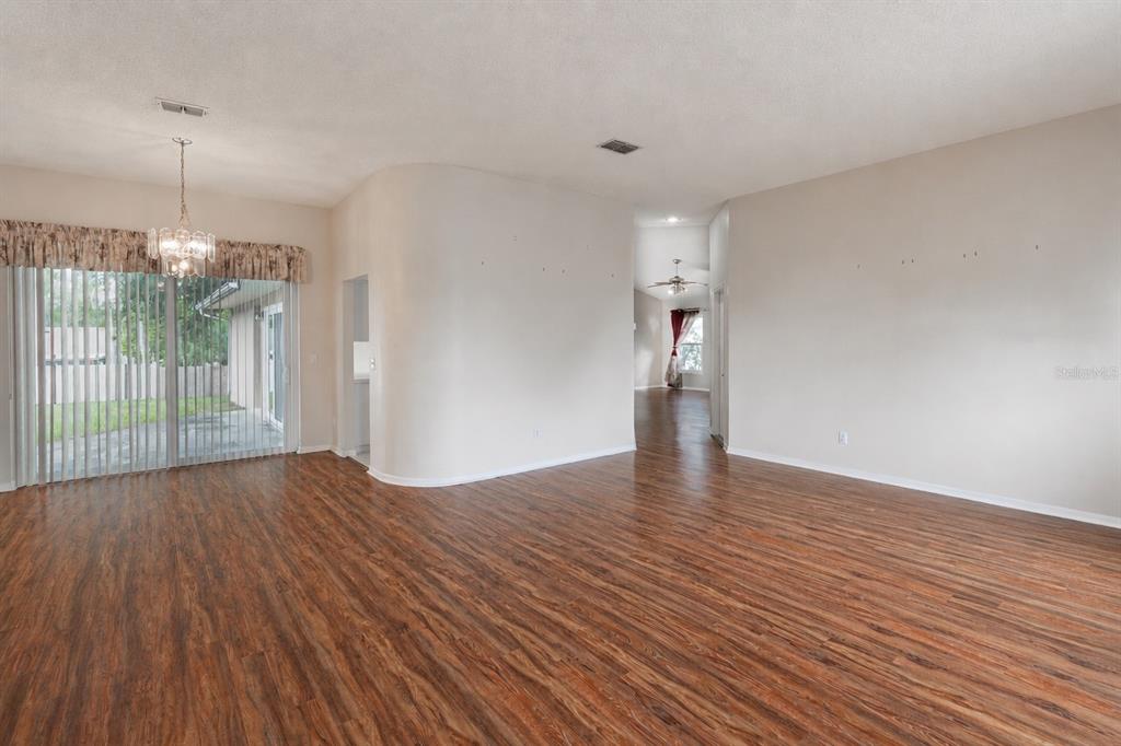 An empty living room features wood-look flooring, a curved wall, and sliding glass patio doors — 10435 CRESTFIELD DRIVE, RIVERVIEW, FL