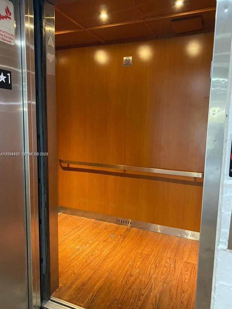 The interior of an elevator features wood-paneled walls, a wood-look floor, and a metal handrail — PLANTATION, FL