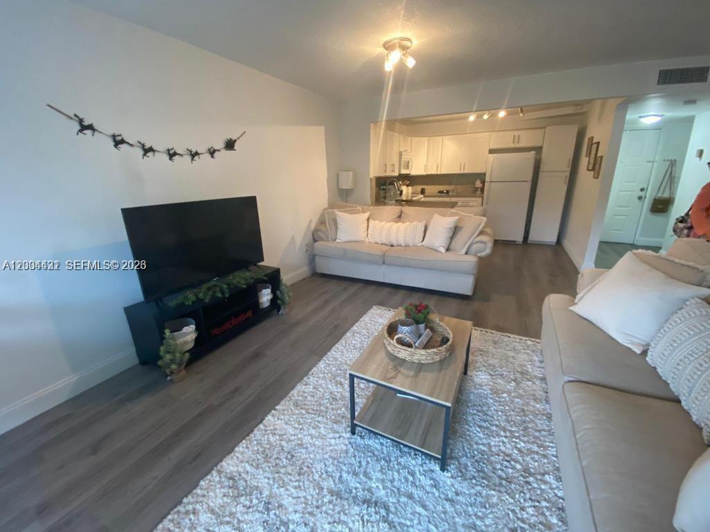This living room features light wood-look flooring, a white sofa, and an open kitchen area — PLANTATION, FL